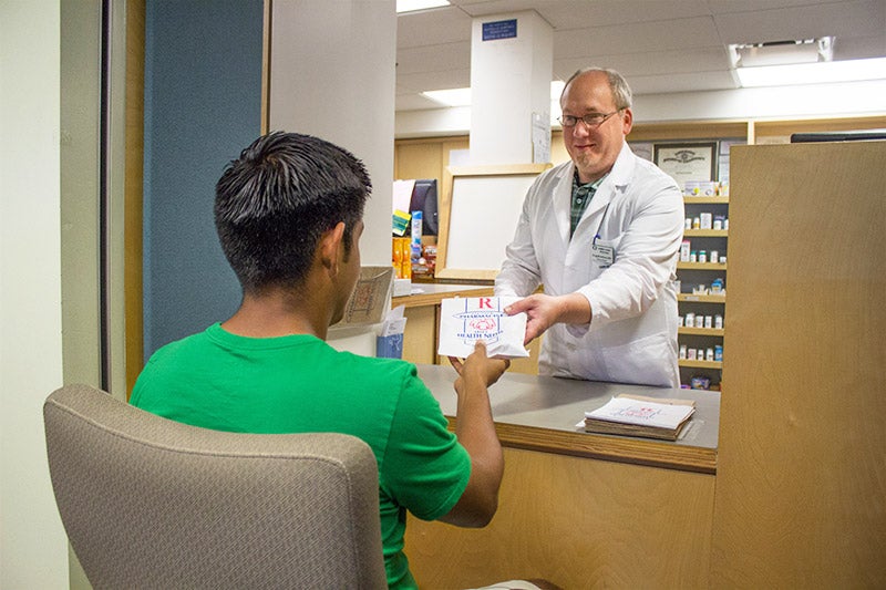 A student picking up a prescription from a pharmacist.